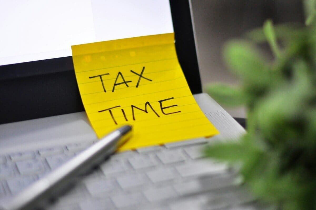 Yellow sticky note with 'TAX TIME' on a laptop keyboard next to a pen
