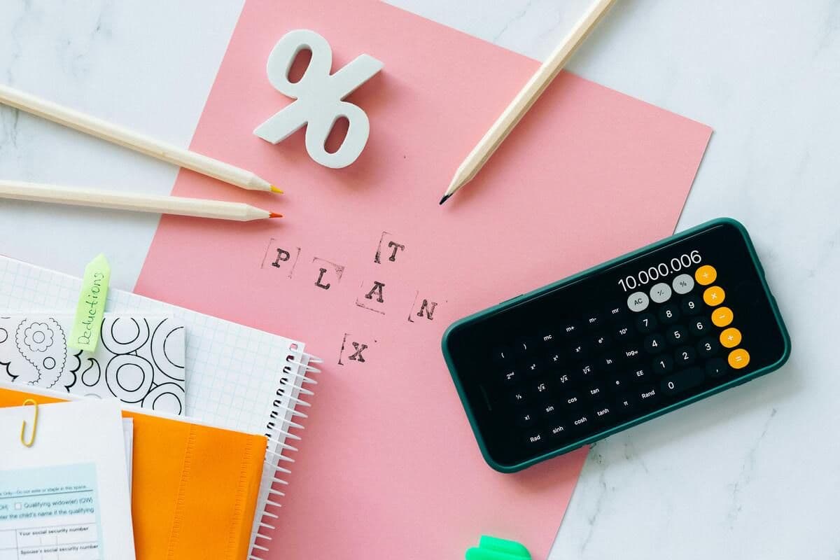 Overhead view of a calculator, percentage sign, pencils, and notebooks on a pink background